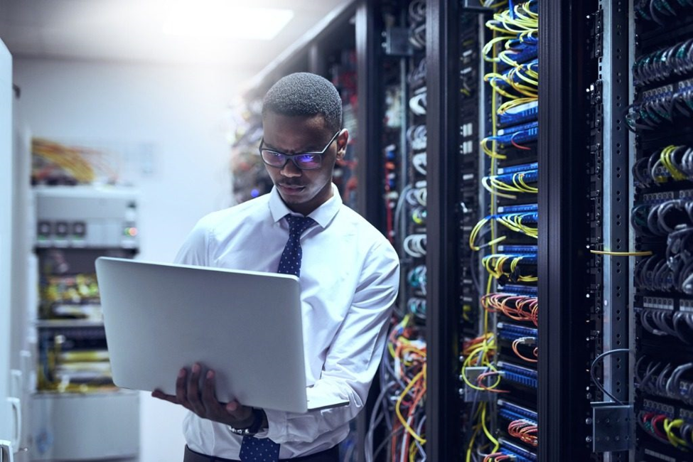 man with laptop standing next to server